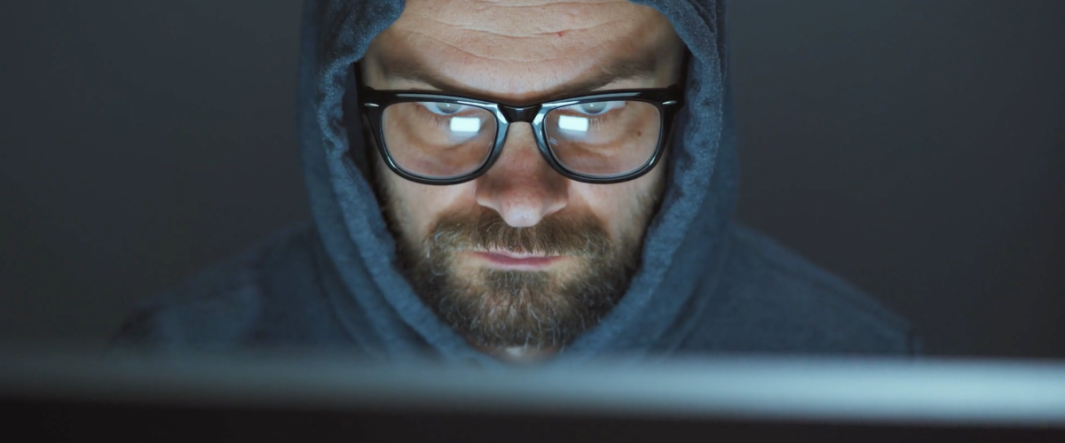 Man wearing glasses and a hoodie looking at a laptop in a dark room